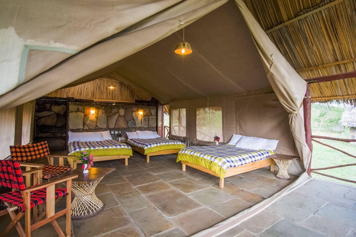 A cozy tent-style accommodation with three beds, a dining area, and a stone wall.