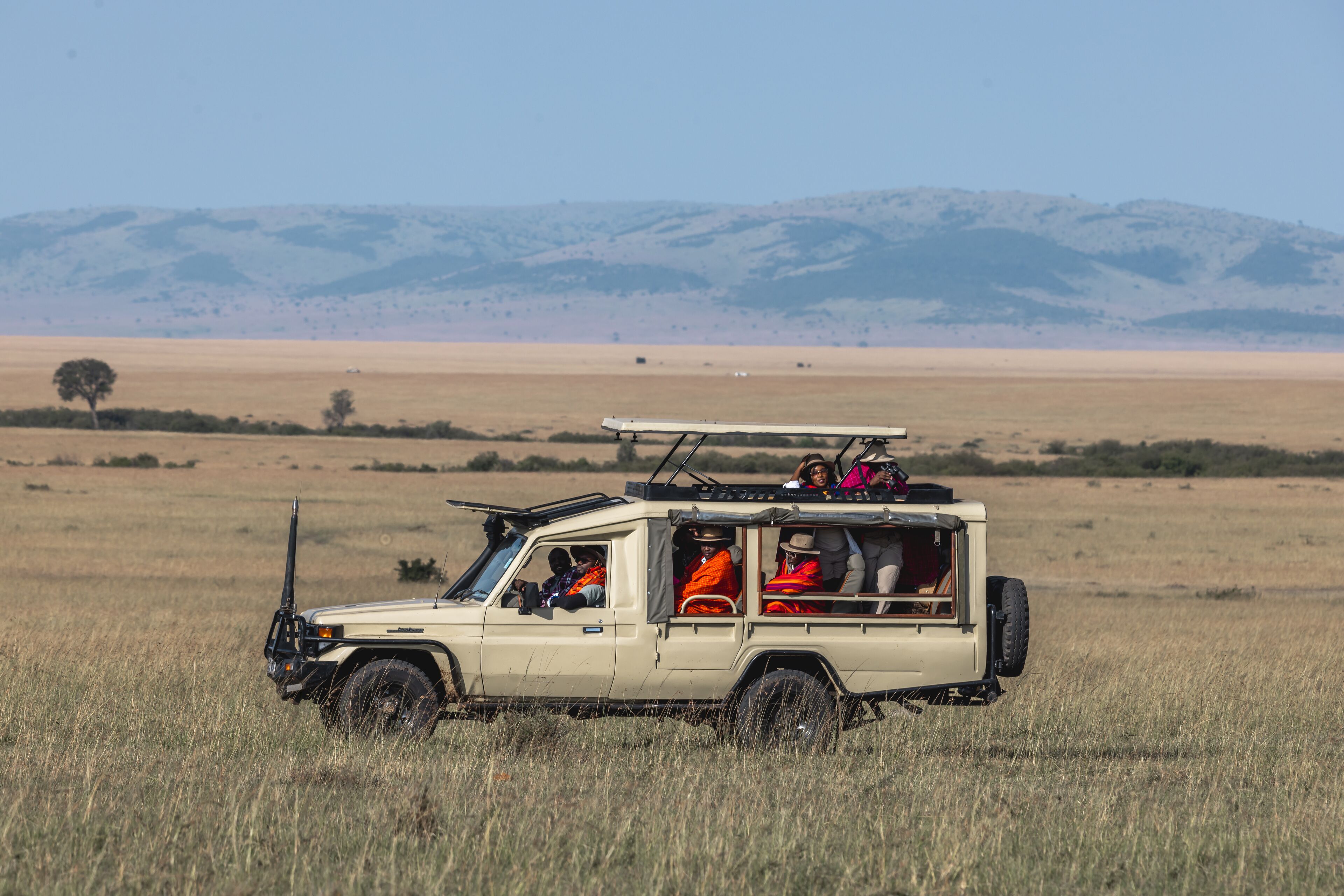 A safari vehicle in a grassy field with mountains in the background.