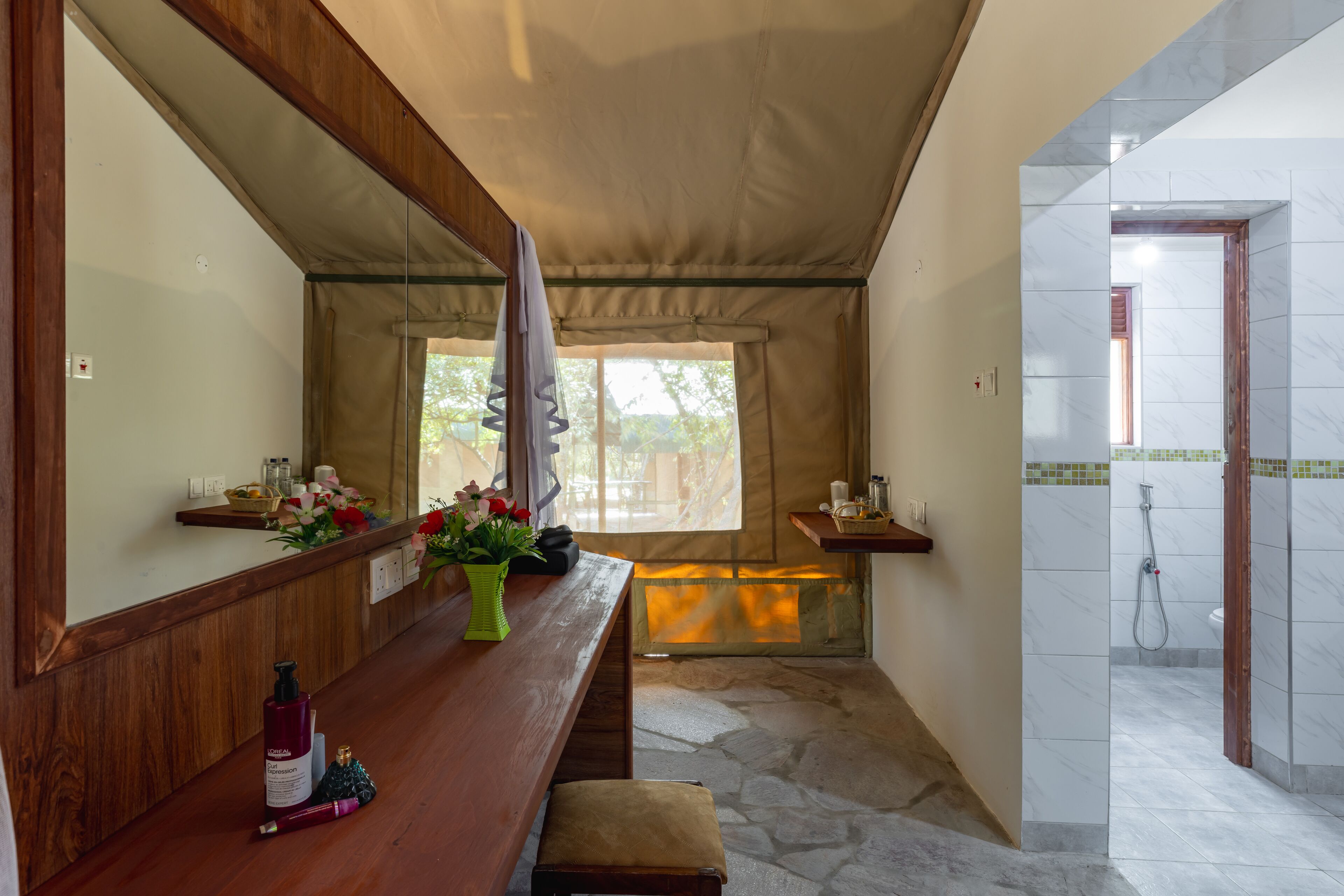 A bathroom with a shower, a bench, a mirror, and a window with curtains.