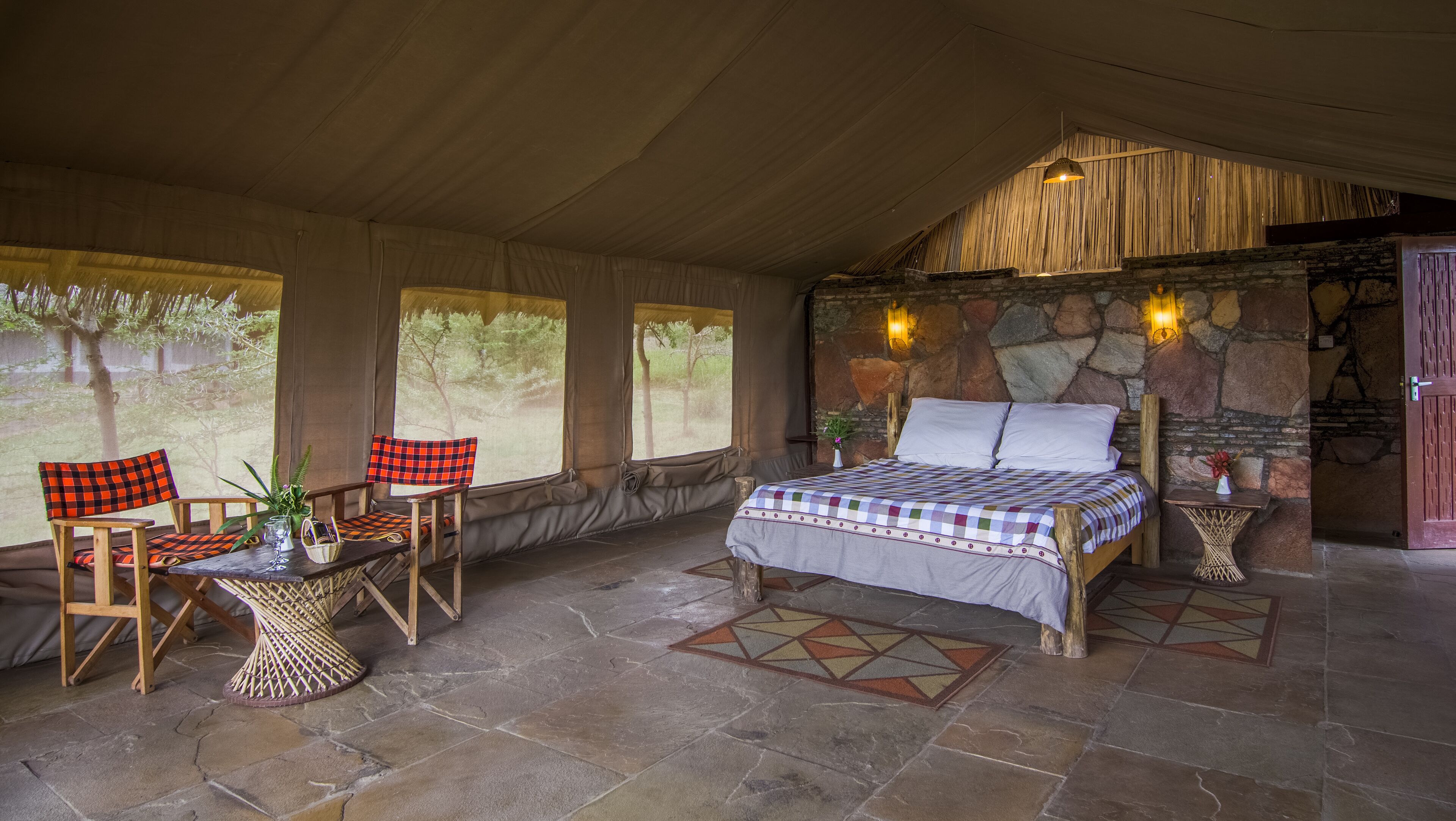 A spacious room with a large bed, a wooden chair, a small table, and a stone wall.