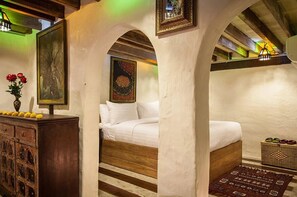 A bedroom with a wooden bed, a nightstand with a vase of flowers, and a wall-mounted shelf with a framed picture.
