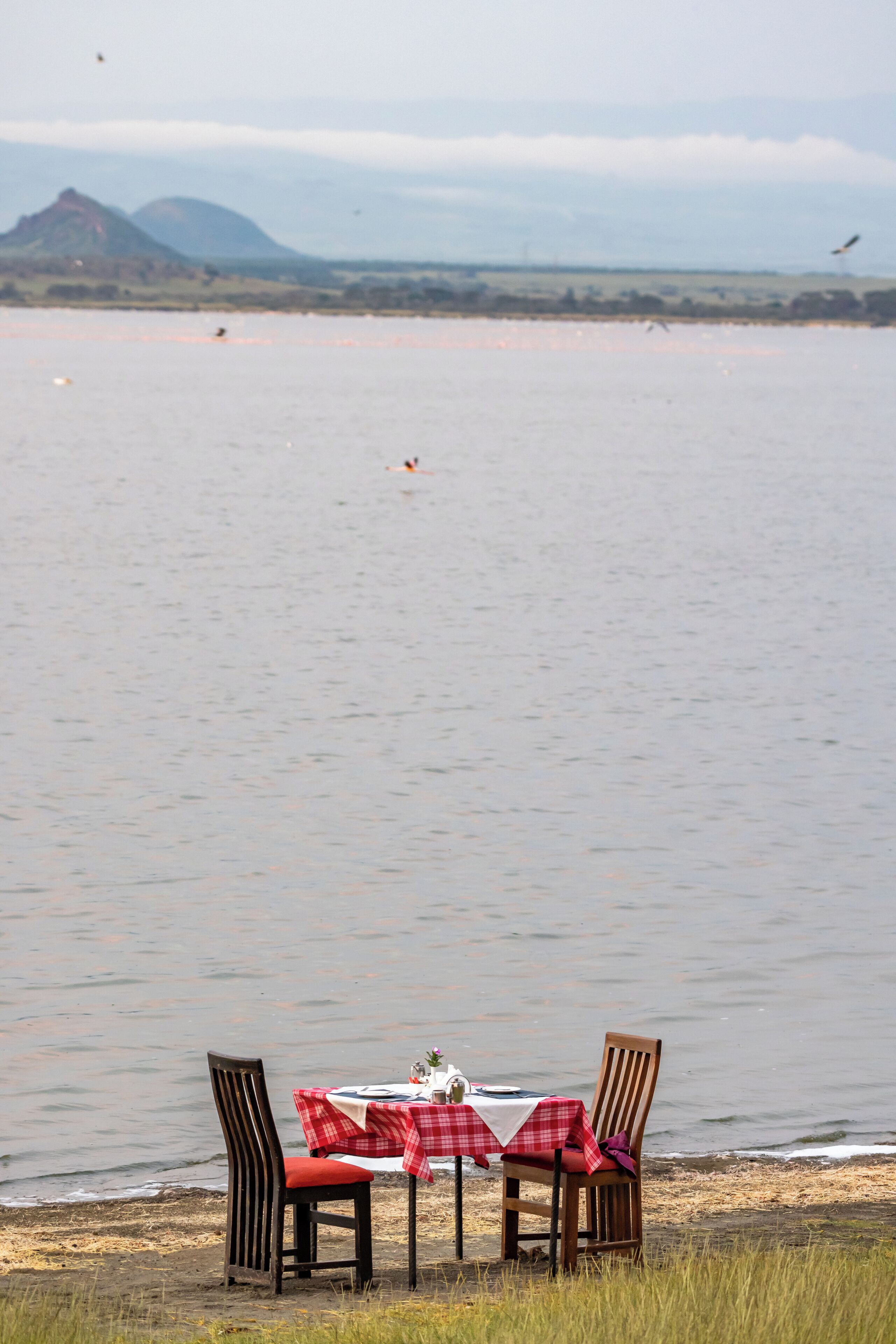 A dining table with a red and white checkered tablecloth, two wooden chairs, and a white table runner.
