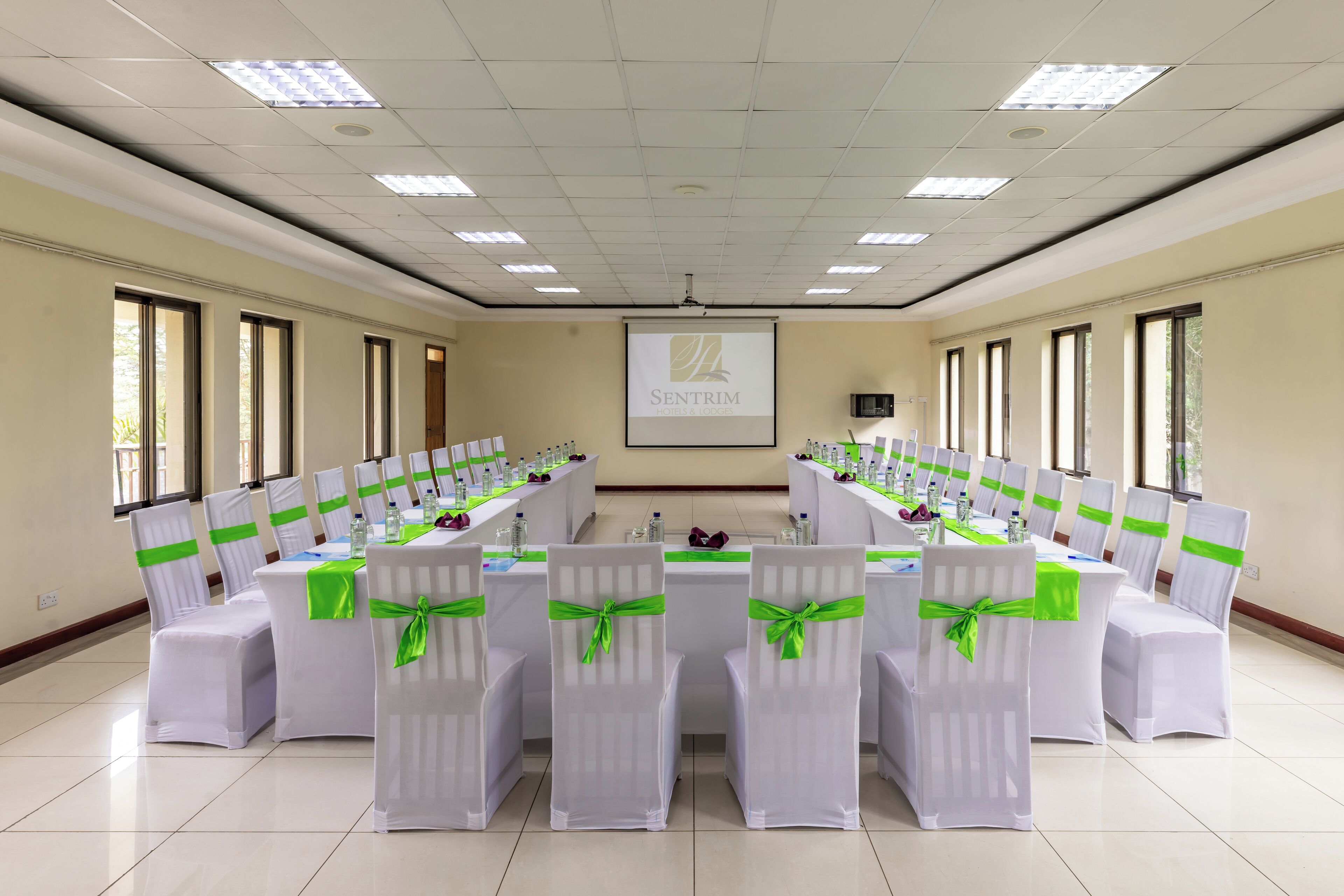 A conference room with a long table, chairs with green sashes, and a projector screen displaying 'SENTRIM'.