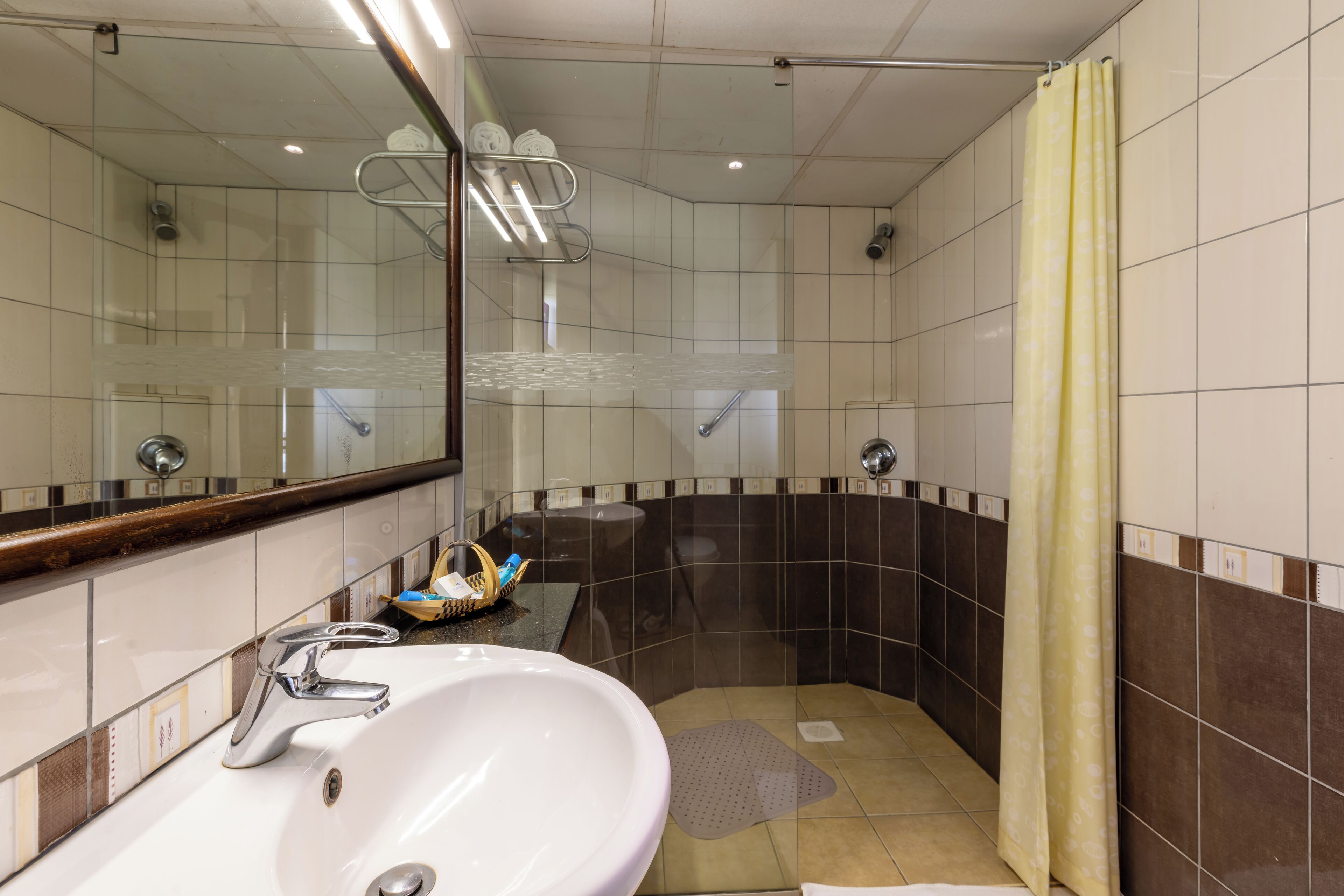 Een badkamer met een wit wastafel, een spiegel, een douche en een geel douchegordijn.