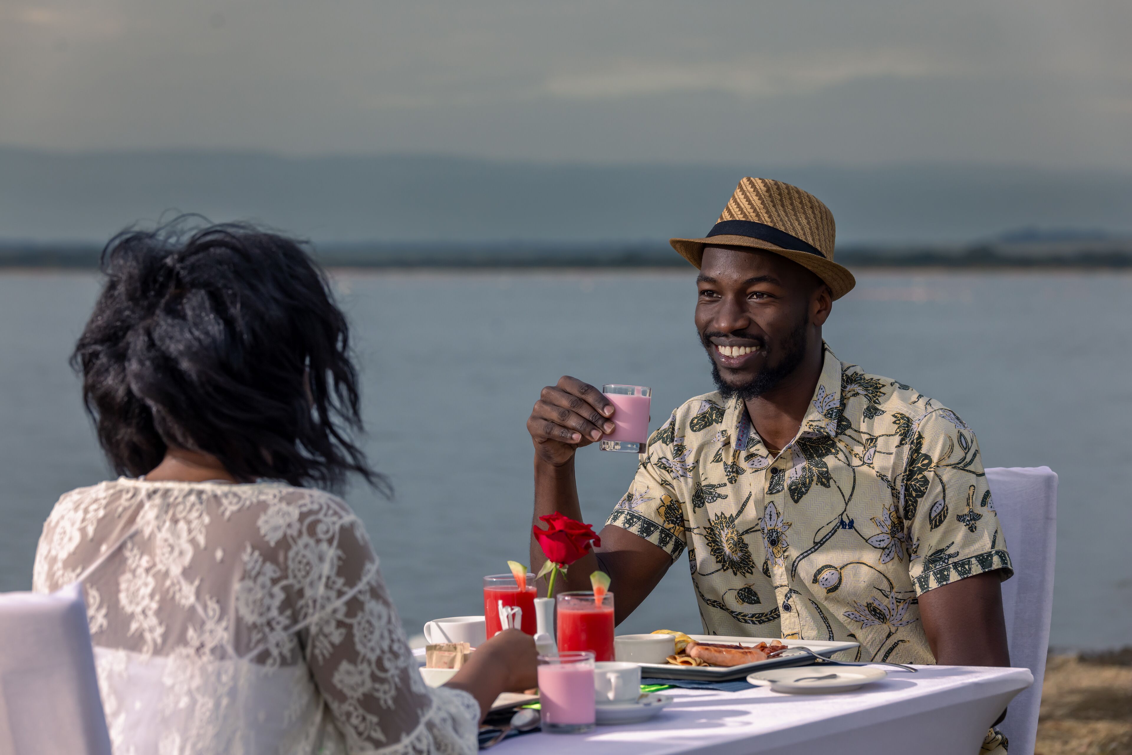 Two people sitting at a table with drinks and food, overlooking a body of water.