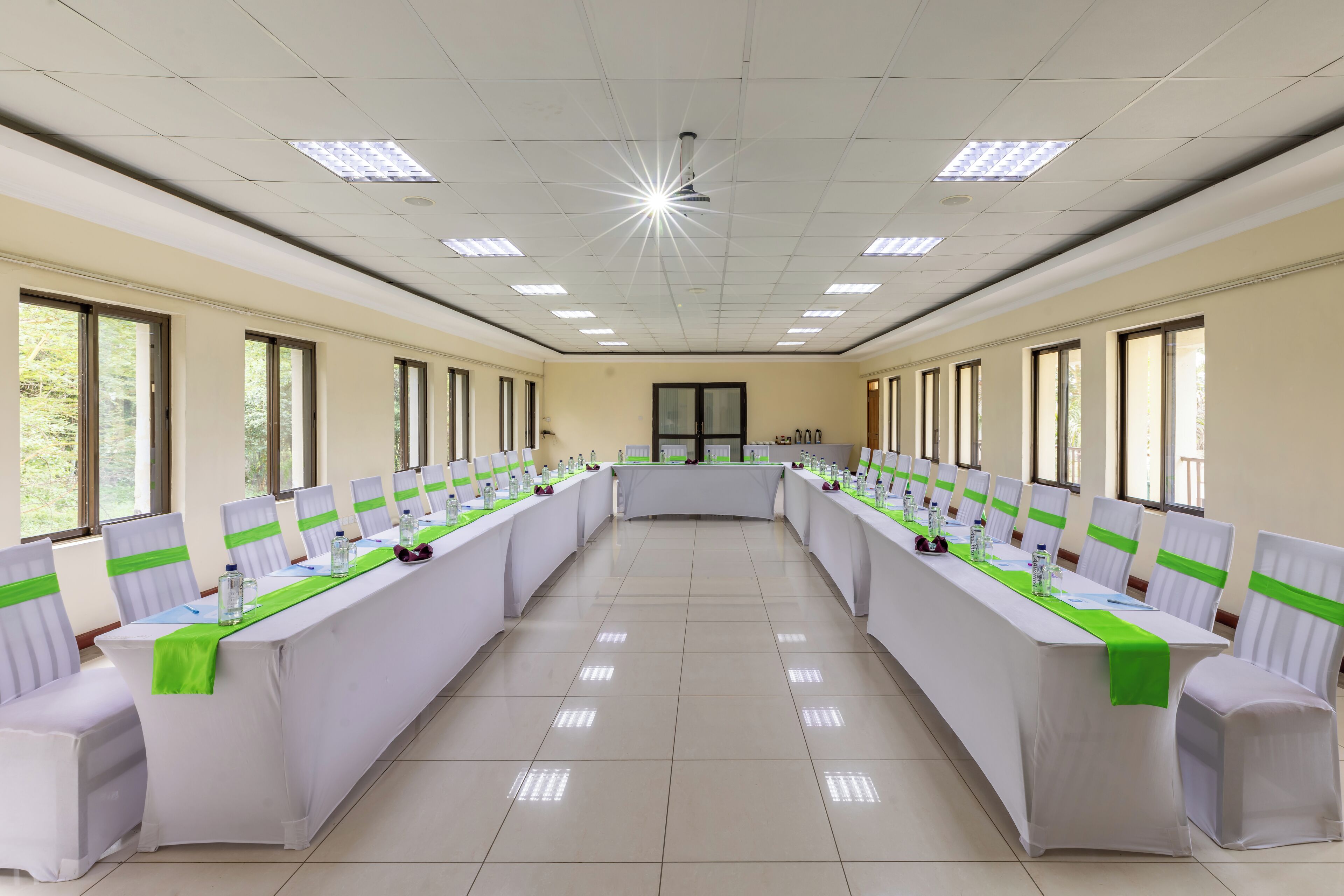 Un salón de conferencias con una larga mesa, sillas con cintas verdes y amplias ventanas.