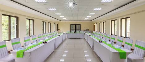 Un salón de conferencias con una larga mesa, sillas con cintas verdes y amplias ventanas.