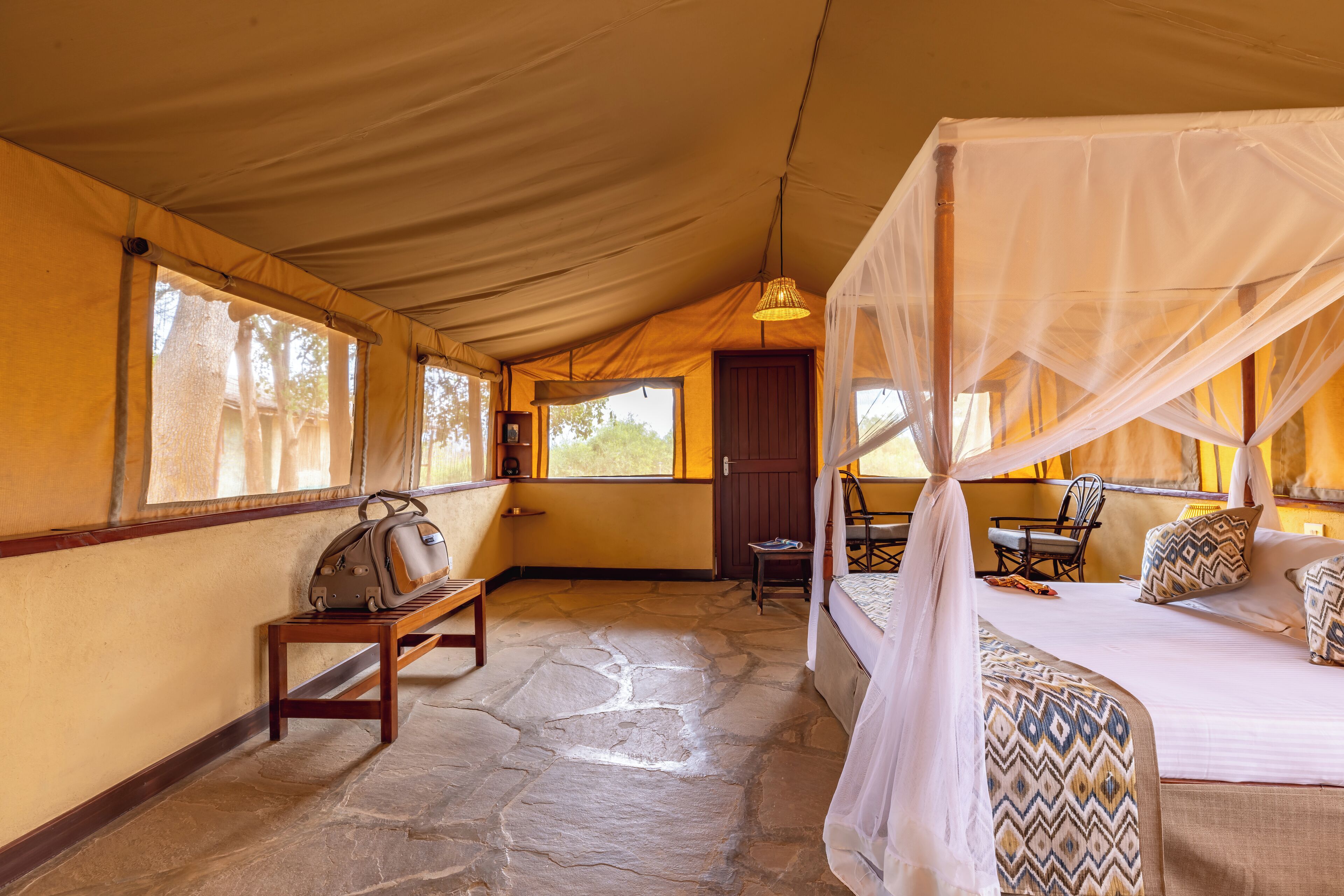 Una habitación con carpa, una cama, un banco y una silla.