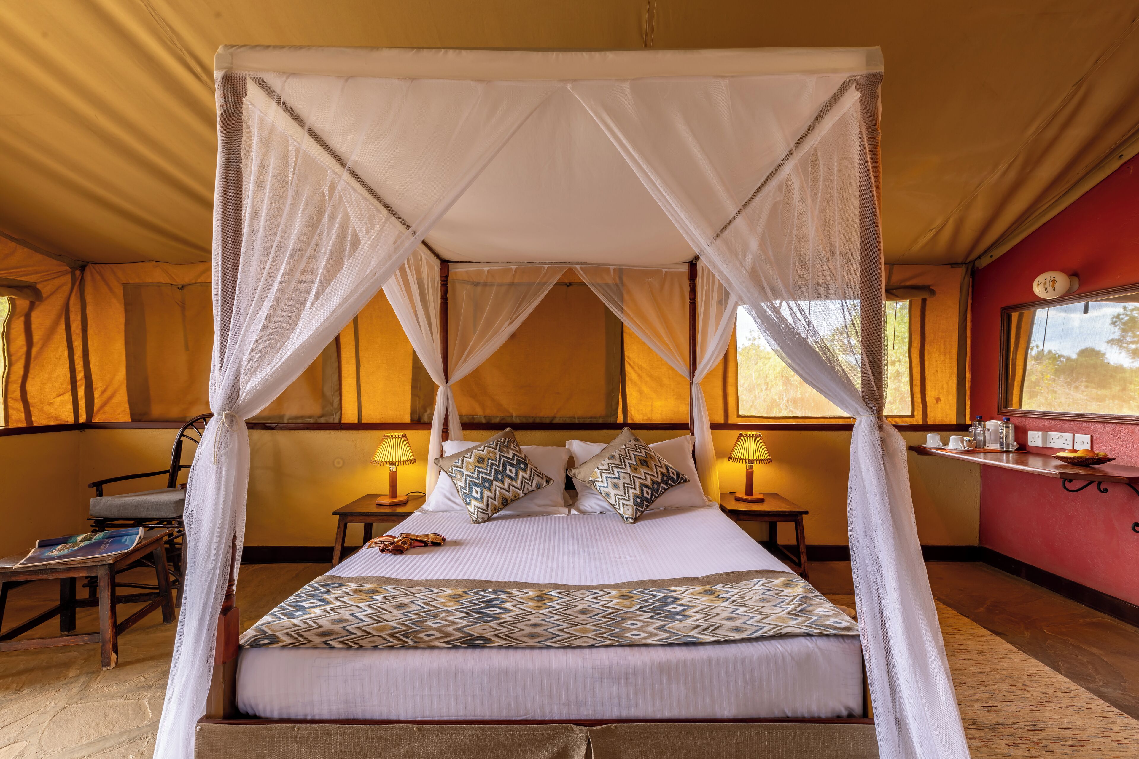 A four-poster bed with a canopy, two bedside tables with lamps, a chair, and a small table with a book.