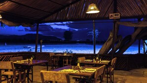An outdoor restaurant with tables and chairs, a 'No Smoking' sign, and a view of a body of water at night. - Sentrim Tsavo Lodge (Voi)