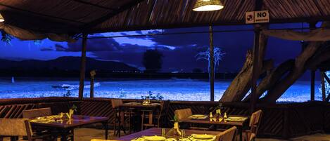Un restaurante al aire libre con mesas y sillas, un letrero que indica 'No Smoking' y vistas a una masa de agua por la noche.