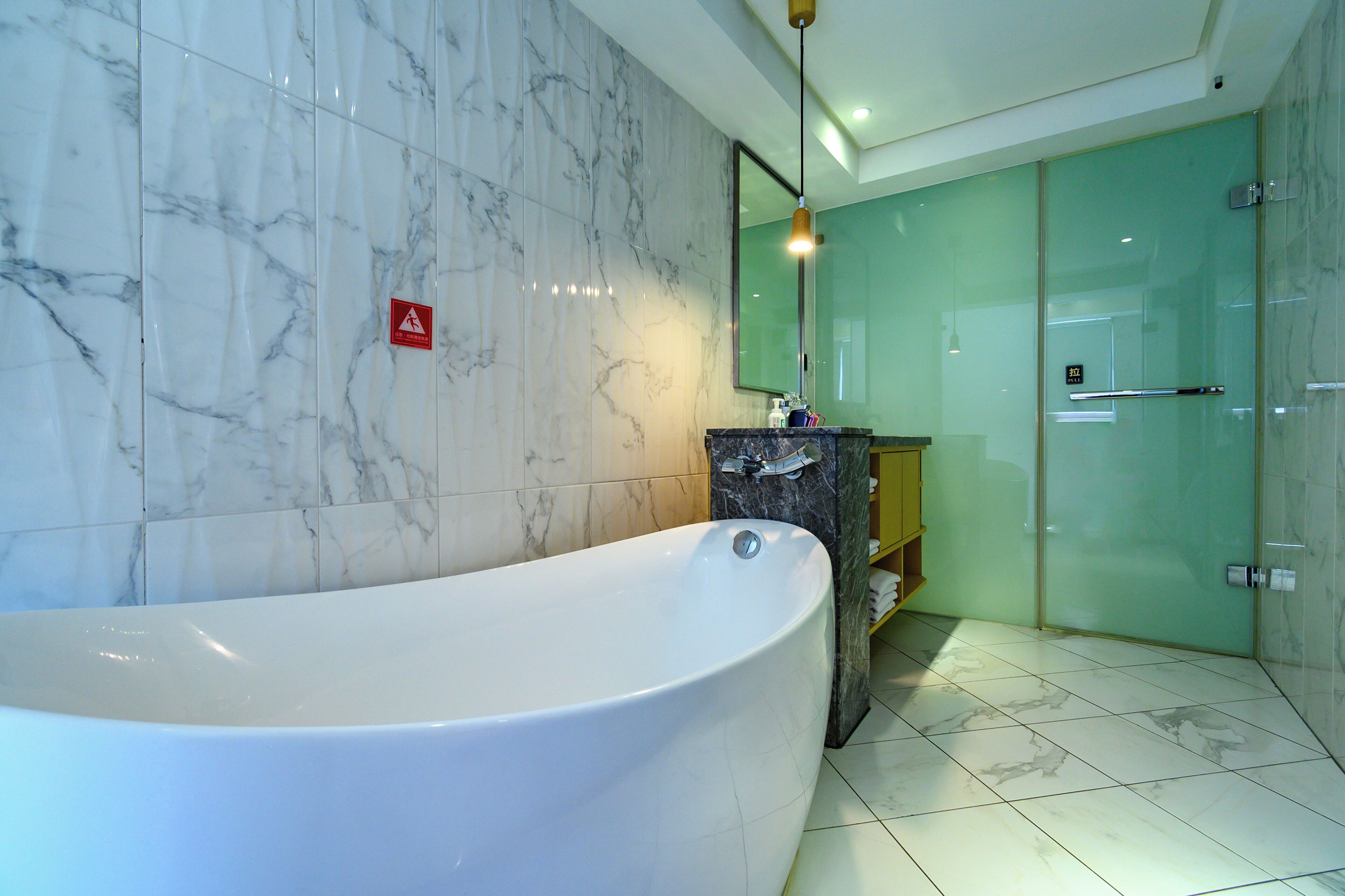 A modern bathroom with a large bathtub, marble walls, a glass shower enclosure, and a wooden vanity.