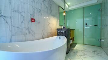 A modern bathroom with a large bathtub, marble walls, a glass shower enclosure, and a wooden vanity.