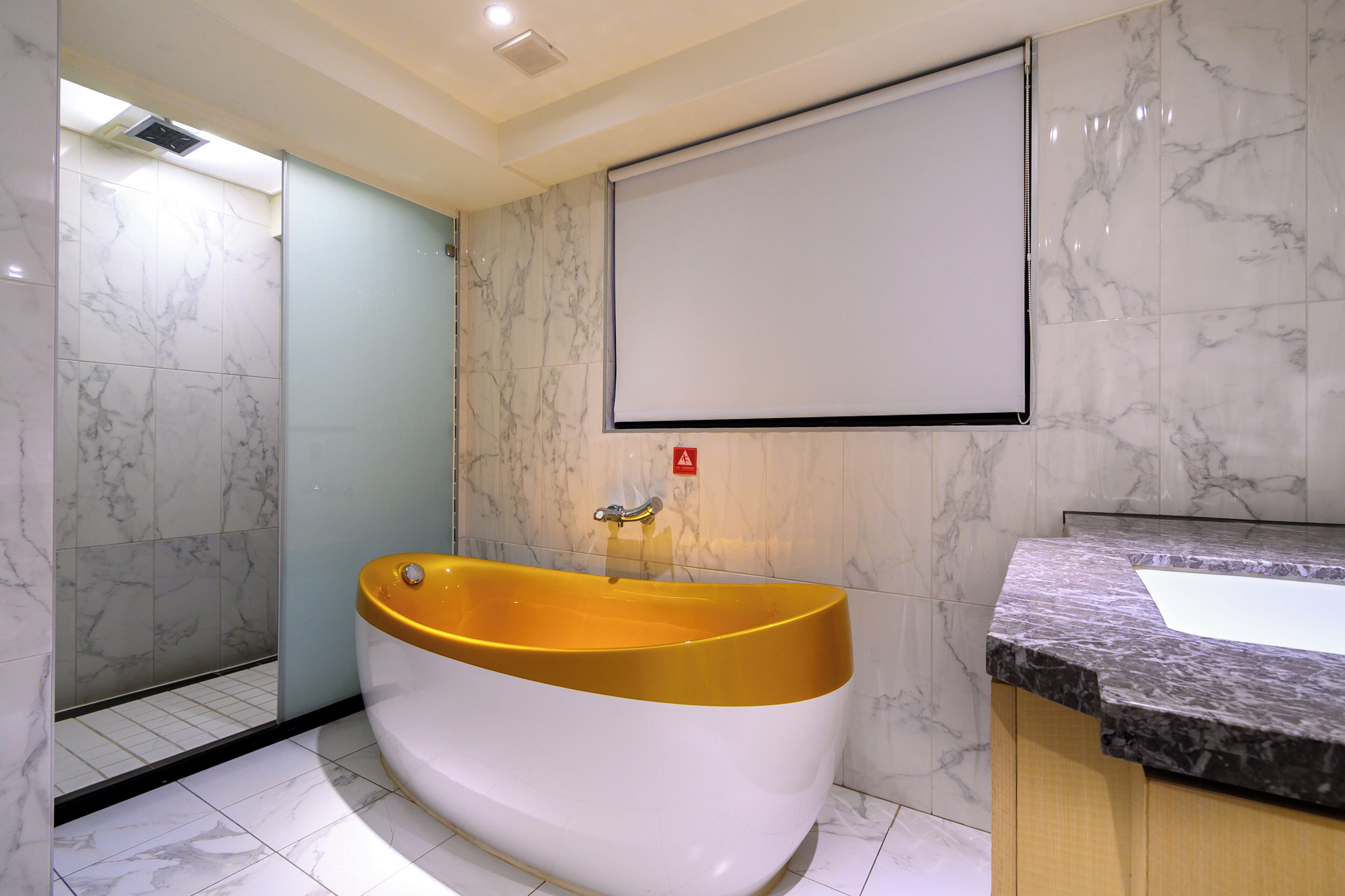 A modern bathroom with a large bathtub, marble walls, and a sink with a granite countertop.