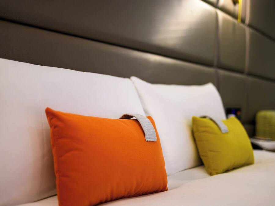 A bed with white bedding and two pillows, one orange and one yellow.