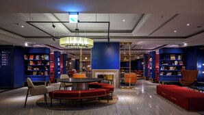 Una biblioteca moderna con una mesa redonda central, asientos rojos y estanterías azules.