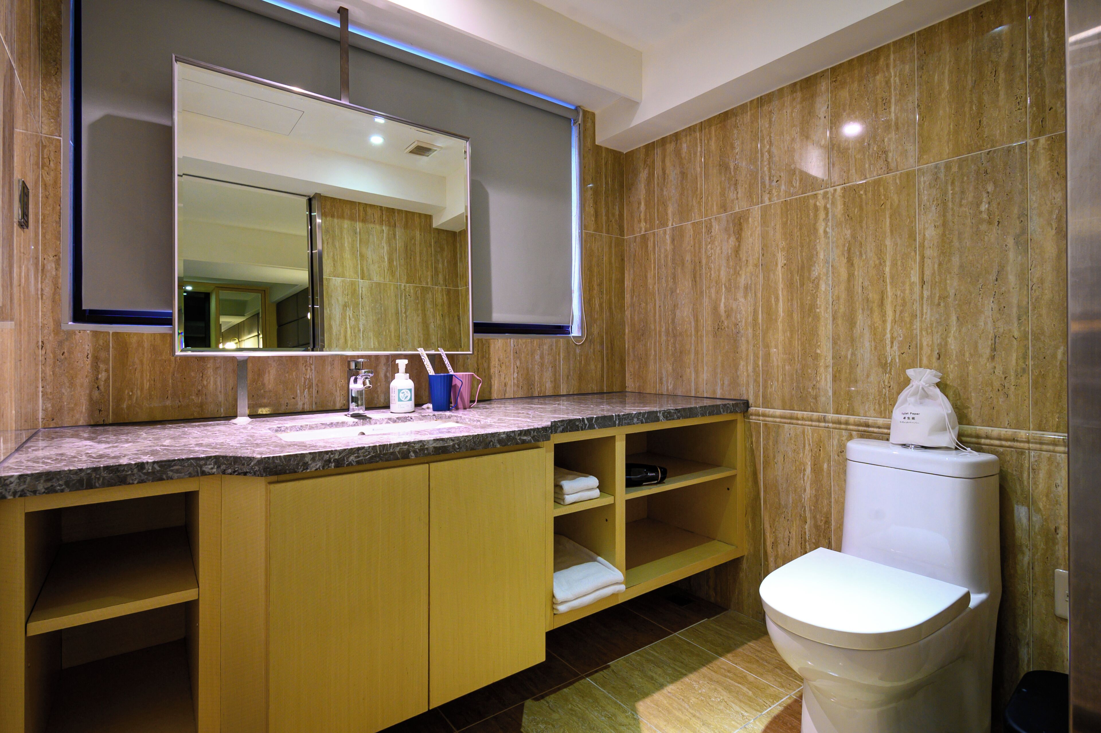 Un baño moderno con encimera de mármol, un espejo grande, inodoro y armarios de madera.