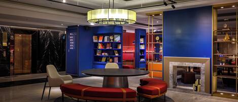 Een moderne lobby met een ronde tafel, rode zitplaatsen, blauwe boekenkasten en een open haard.