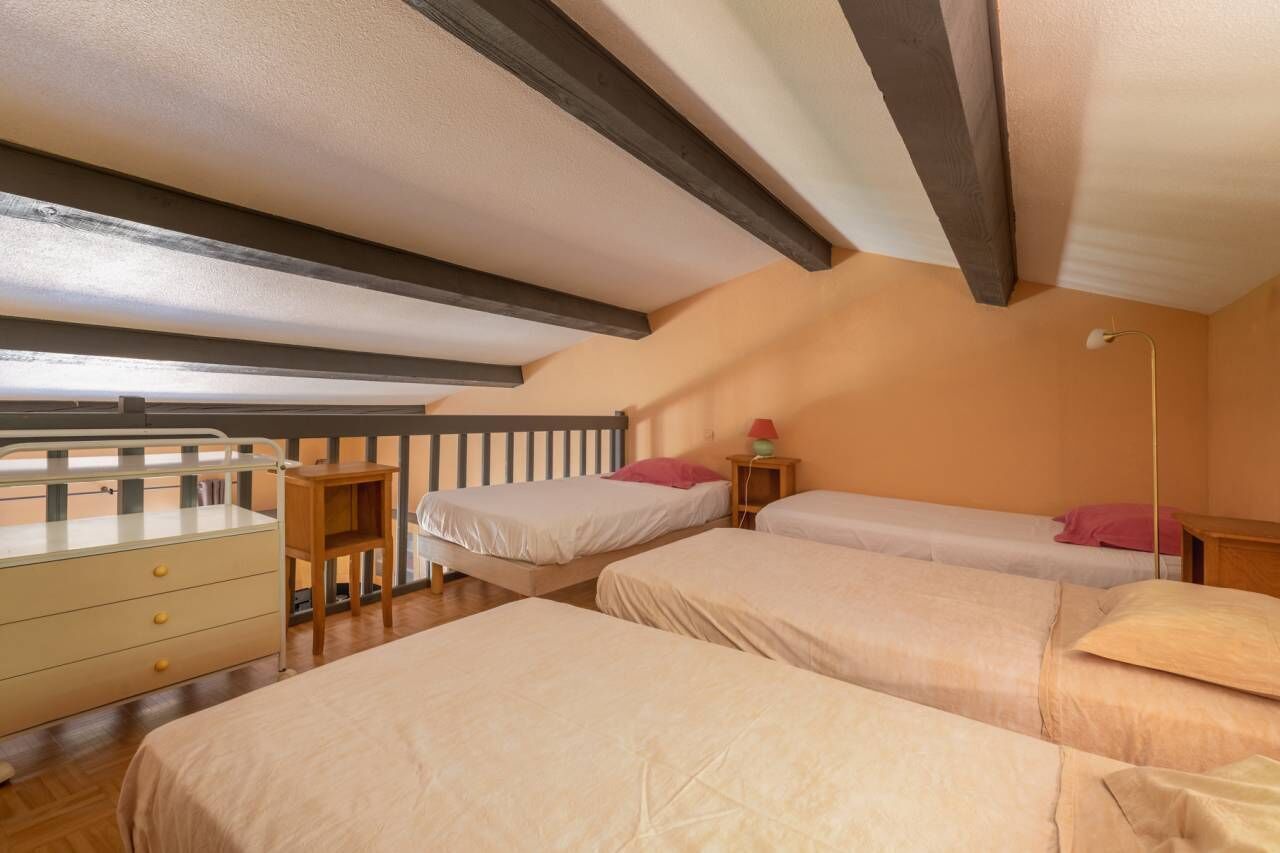 A bedroom with three beds, a wooden dresser, and a small table with a lamp.