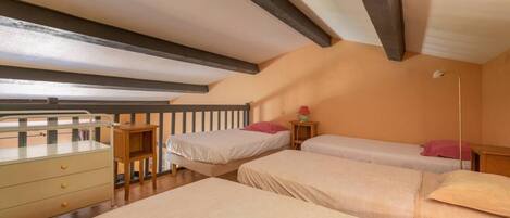 A bedroom with three beds, a wooden dresser, and a small table with a lamp.