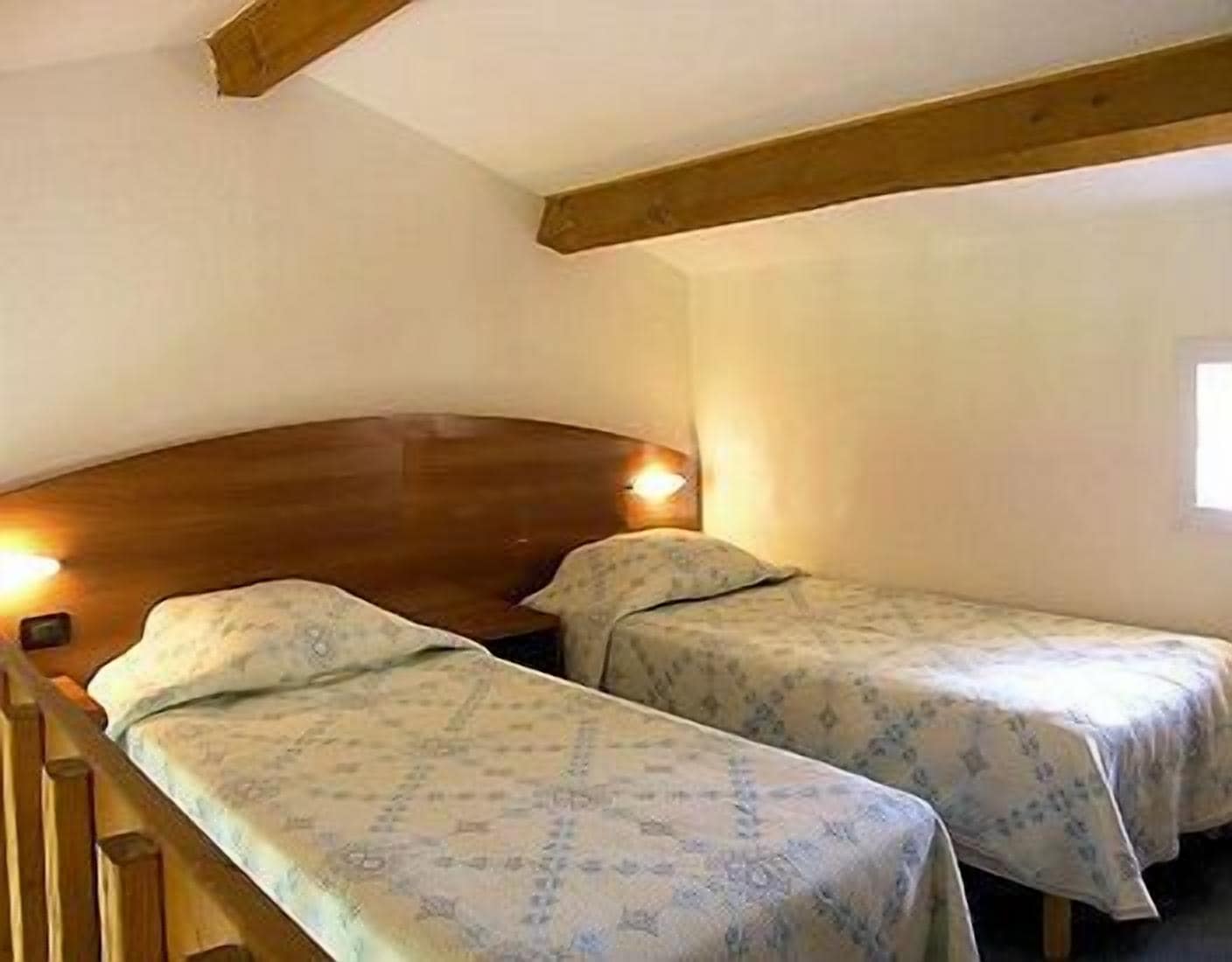 A small room with two single beds, wooden headboards, and a sloped ceiling.