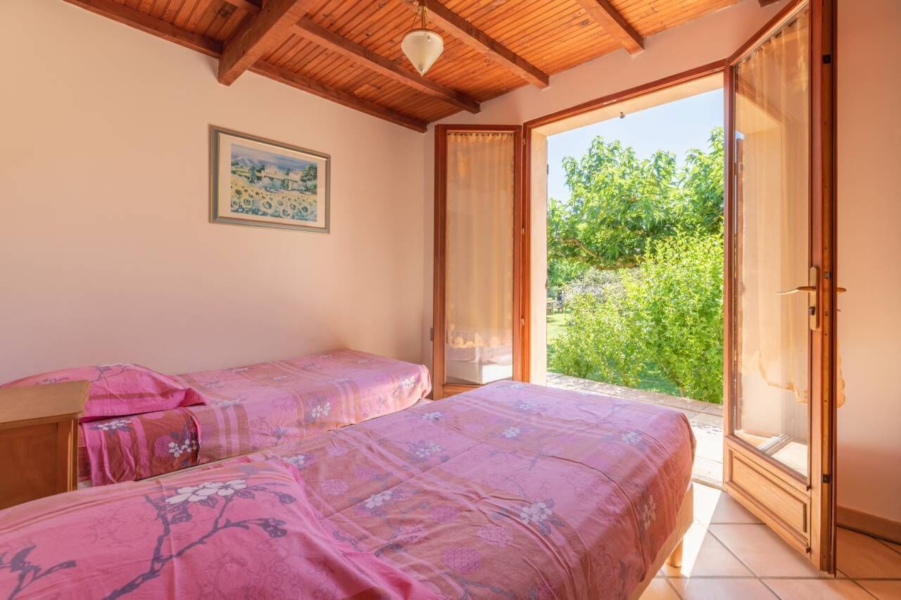 A bedroom with two beds, a wooden ceiling, a window, and a door leading to a balcony.