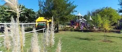 Un espacio al aire libre con césped, que incluye un parque infantil, una estructura amarilla y un pabellón.