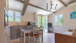 A kitchen with a dining table, chairs, a microwave, and a coffee maker. There is a sofa and a TV in the living area.