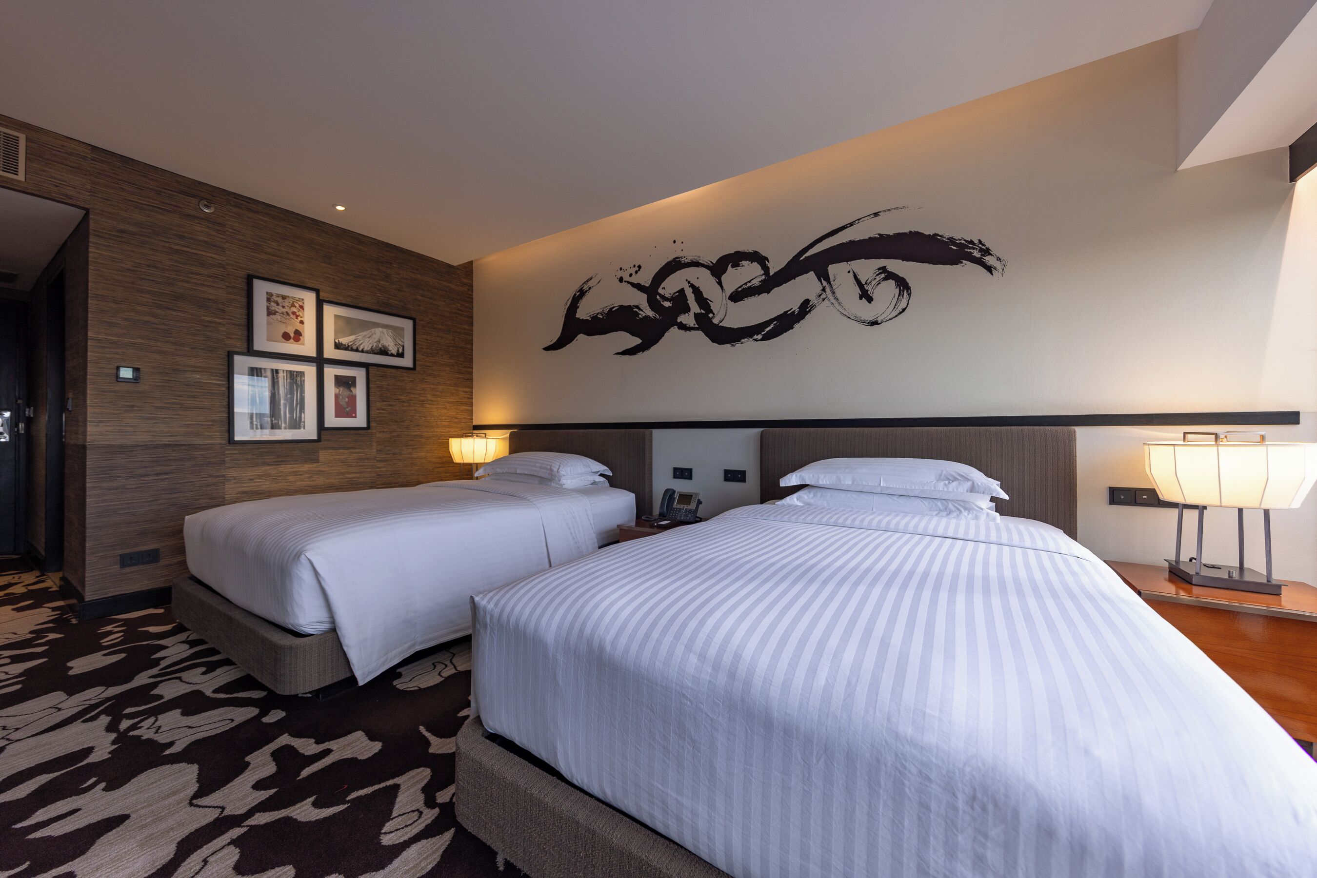 Habitación de hotel con dos camas, una gran obra de arte abstracta en la pared y una alfombra estampada.