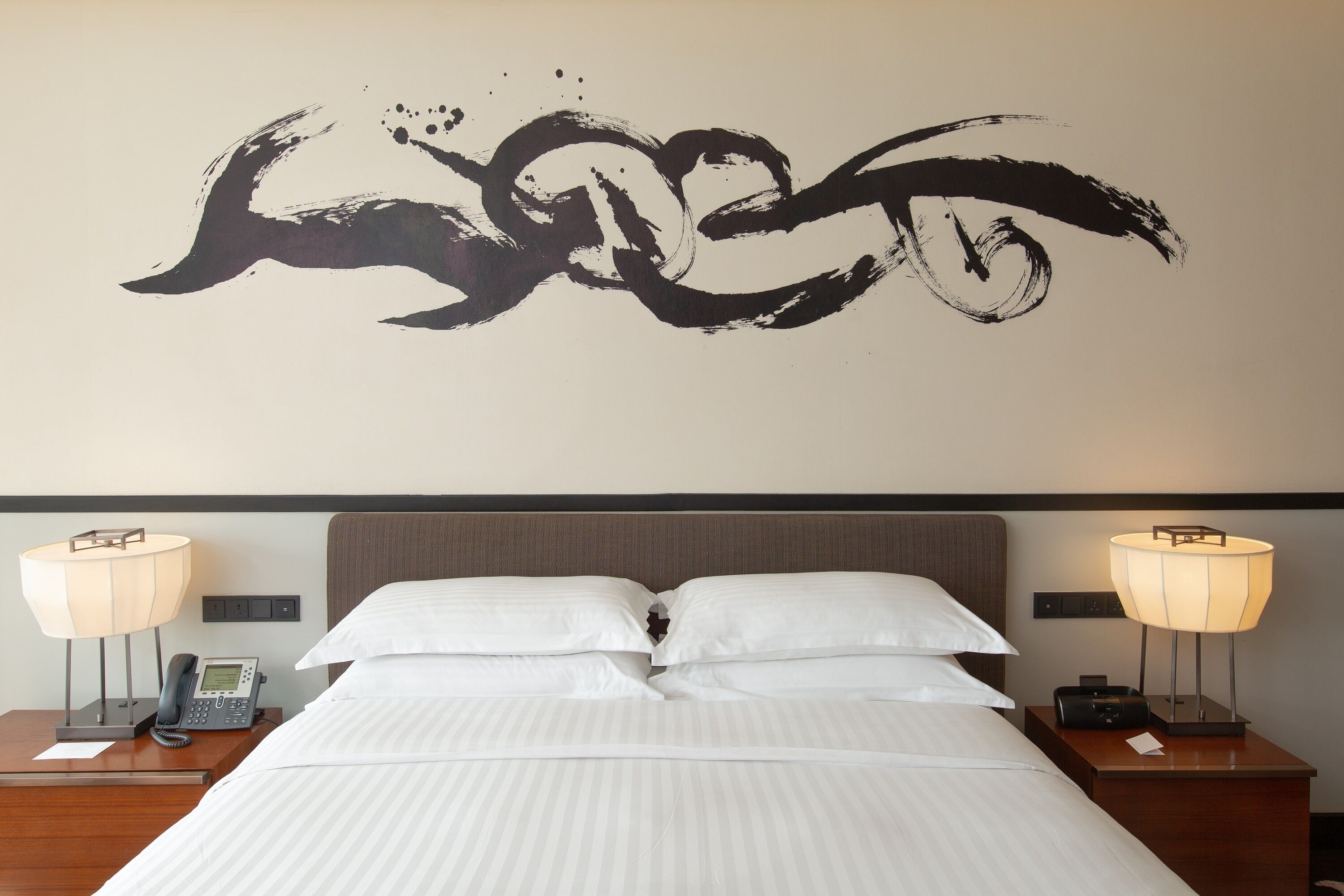 Habitación de hotel con cama, dos mesitas de noche, un teléfono en la pared y una obra de arte en la pared.