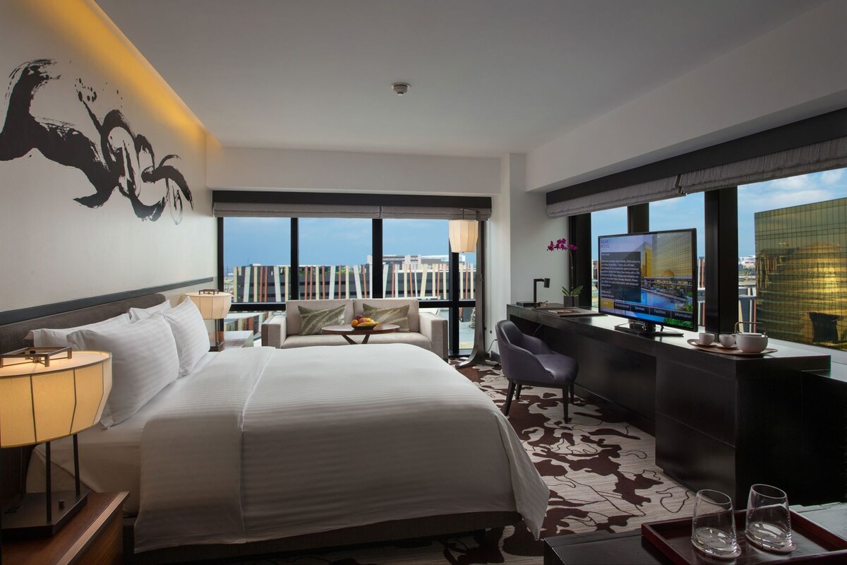 Habitación de hotel con cama, escritorio, televisión y vista a la ciudad.