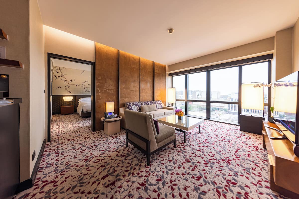 Una habitación de hotel con un ventanal grande, un sofá, una mesa de centro y una alfombra estampada.