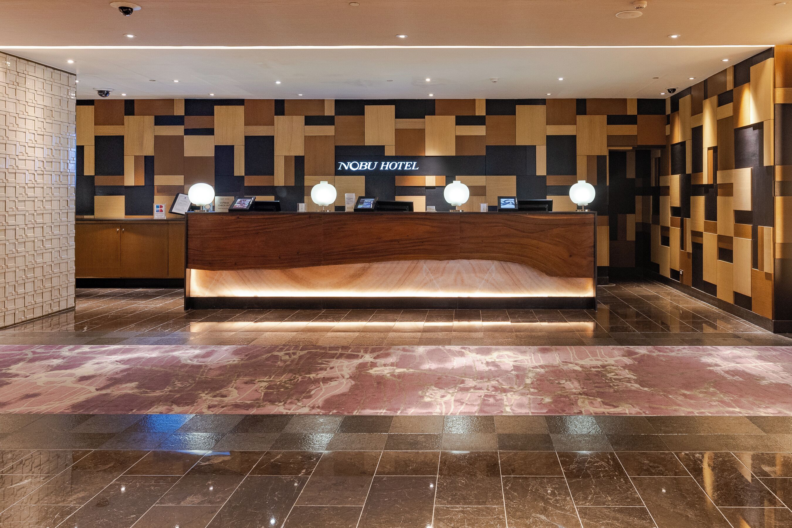 En hotellreception med modern design, en skylt med texten ”Nobu Hotel” och ett marmorgolv.