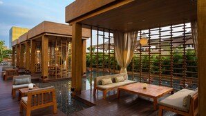 Um deck de madeira com assentos e piscina, cercado por divisórias de madeira e vegetação.