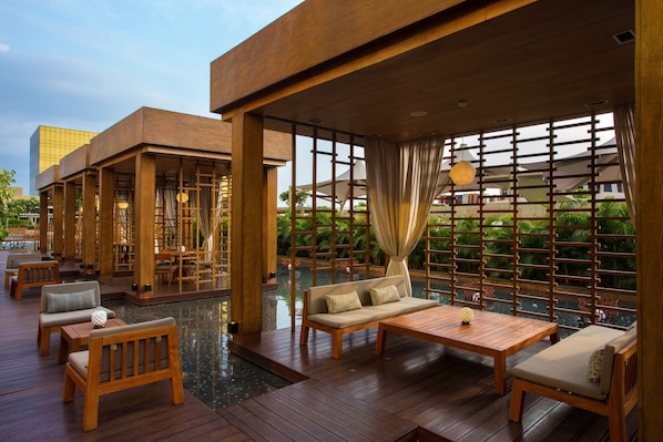 A wooden deck with seating and a pool, surrounded by wooden partitions and greenery.