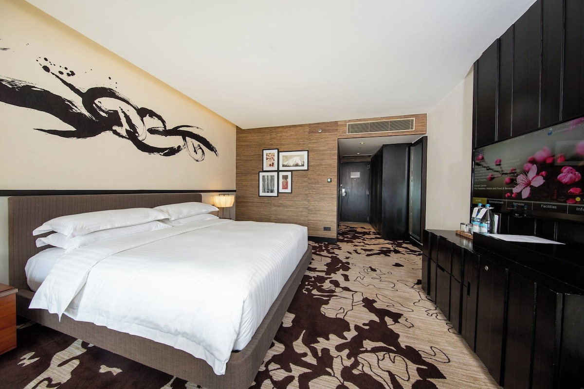 Ein Hotelzimmer mit Bett, Fernseher, einer Wand mit Kunstwerken und Teppich.