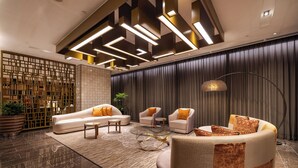 Um hall moderno com sofá de canto, poltronas, mesa de centro de vidro e um abajur decorativo.