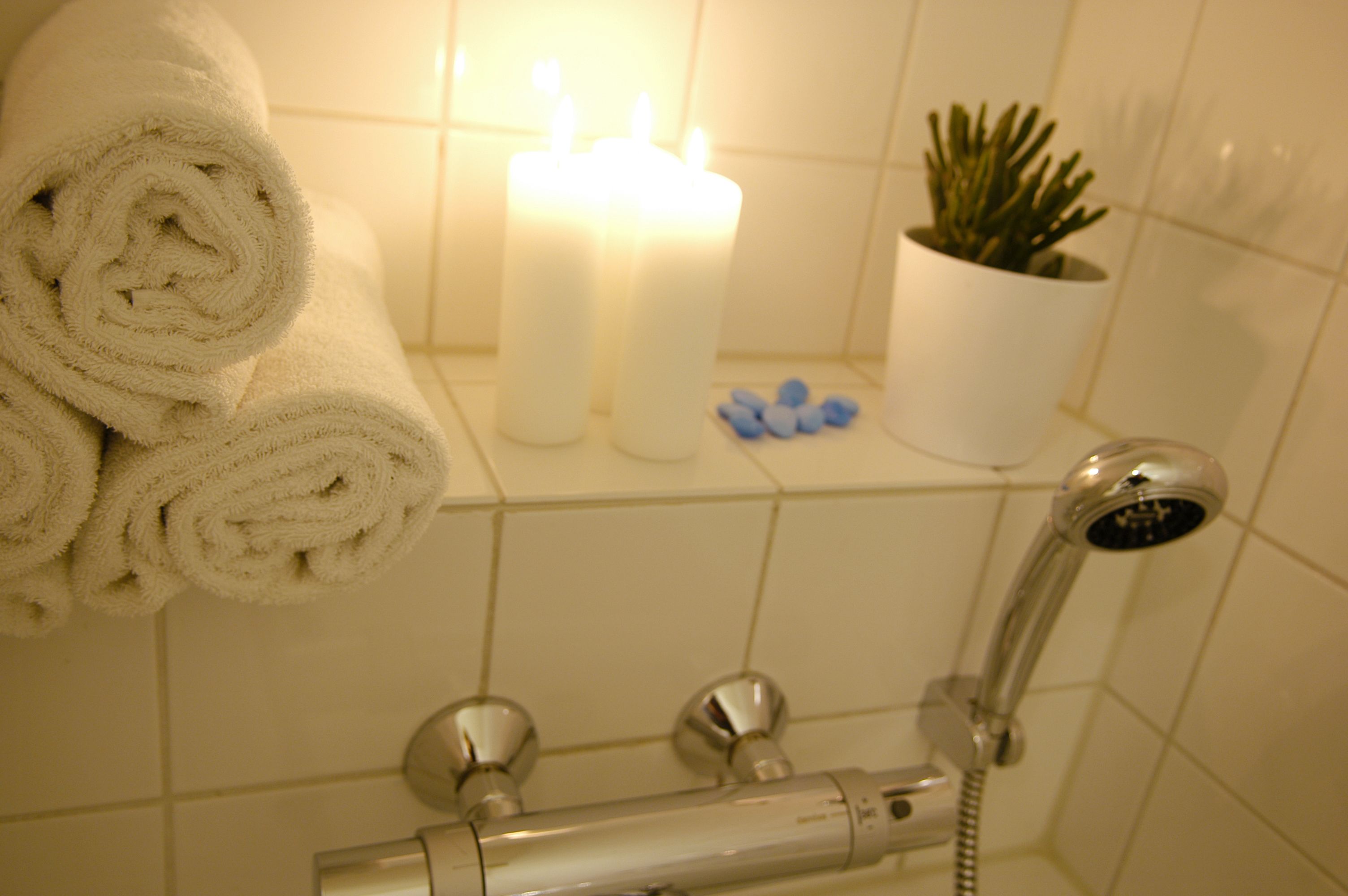 A bathroom with a shower, a towel rack with rolled towels, a lit candle, and a potted plant.