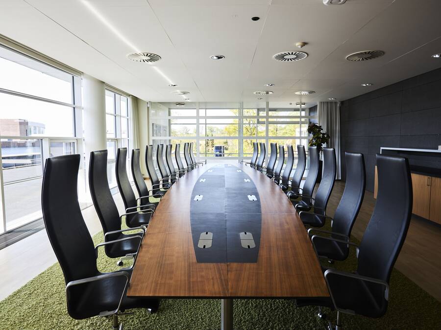 Une salle de conférence dotée d’une longue table et de rangées de chaises, de grandes fenêtres et d’un plafond au design moderne.