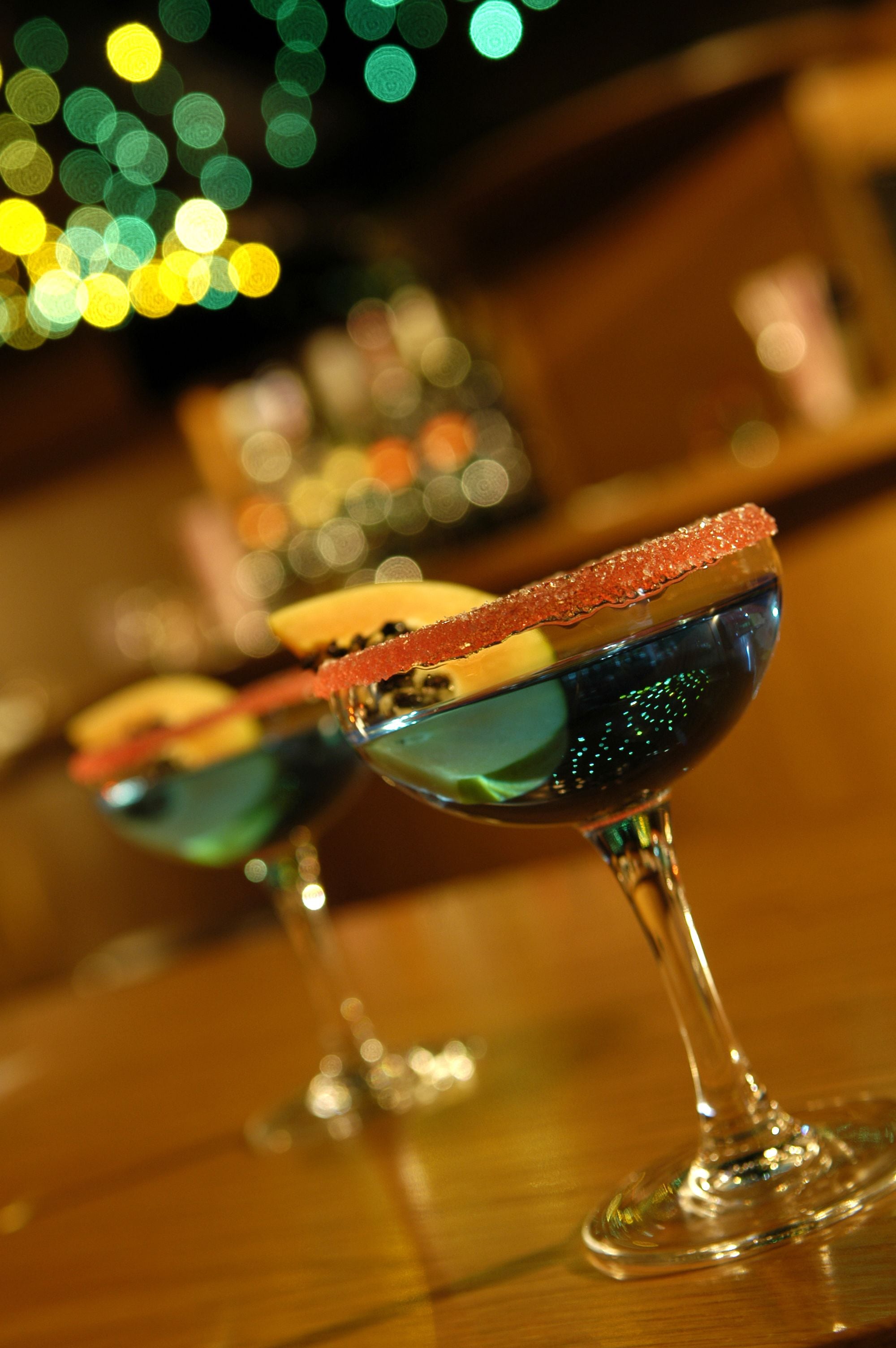 Three cocktail glasses with a salted rim on a wooden bar counter.