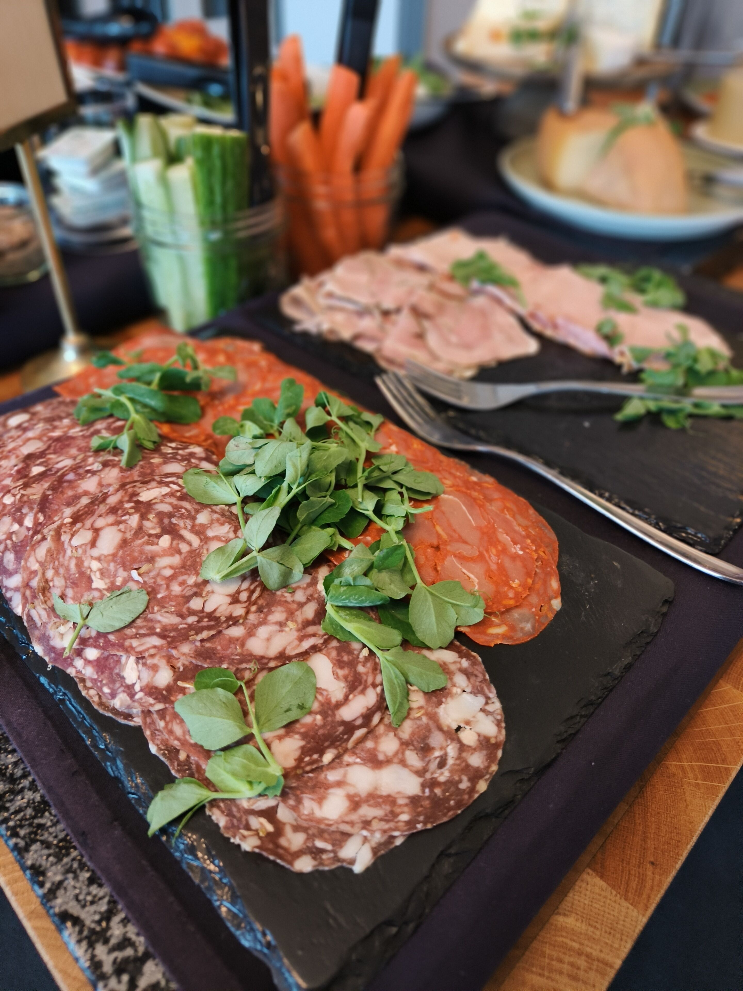 A charcuterie board with various meats and greens on a slate board.