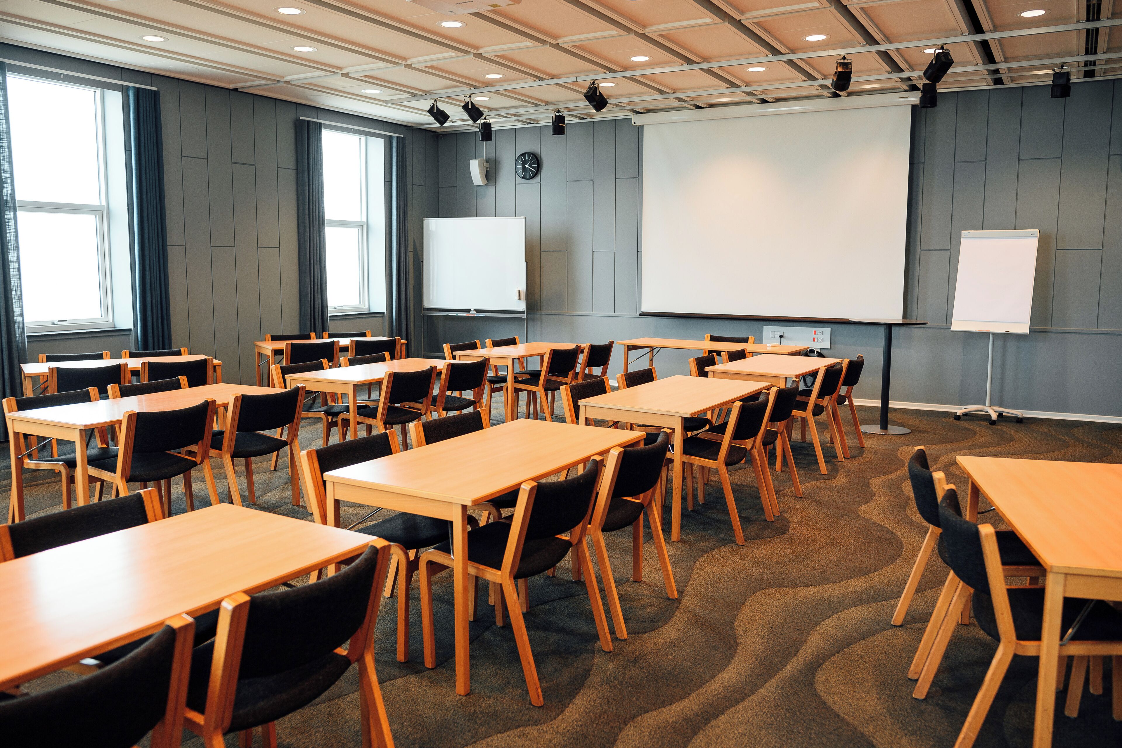 Un salón de conferencias con varias mesas y sillas, amplias ventanas y una pizarra.
