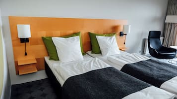 Et hotelværelse med to senge, en træsenggavl, grønne og hvide puder, en sort stol og en lampe på væggen.