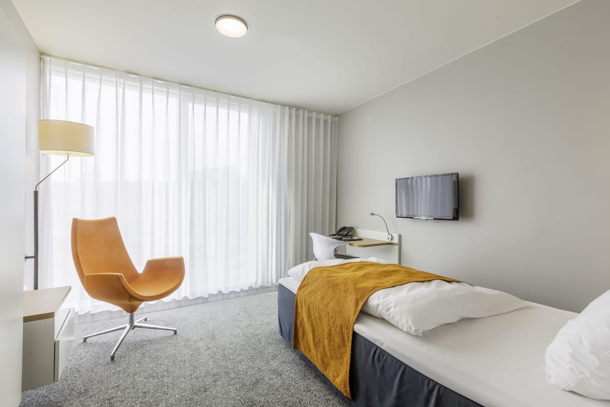 A hotel room with a bed, a chair, a desk, a lamp, and a TV.