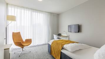 Ein Hotelzimmer mit Bett, Sessel, Schreibtisch, Lampe und Fernseher.