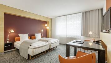 Habitación de hotel con dos camas, un escritorio, una silla, un televisor y una ventana con cortinas.