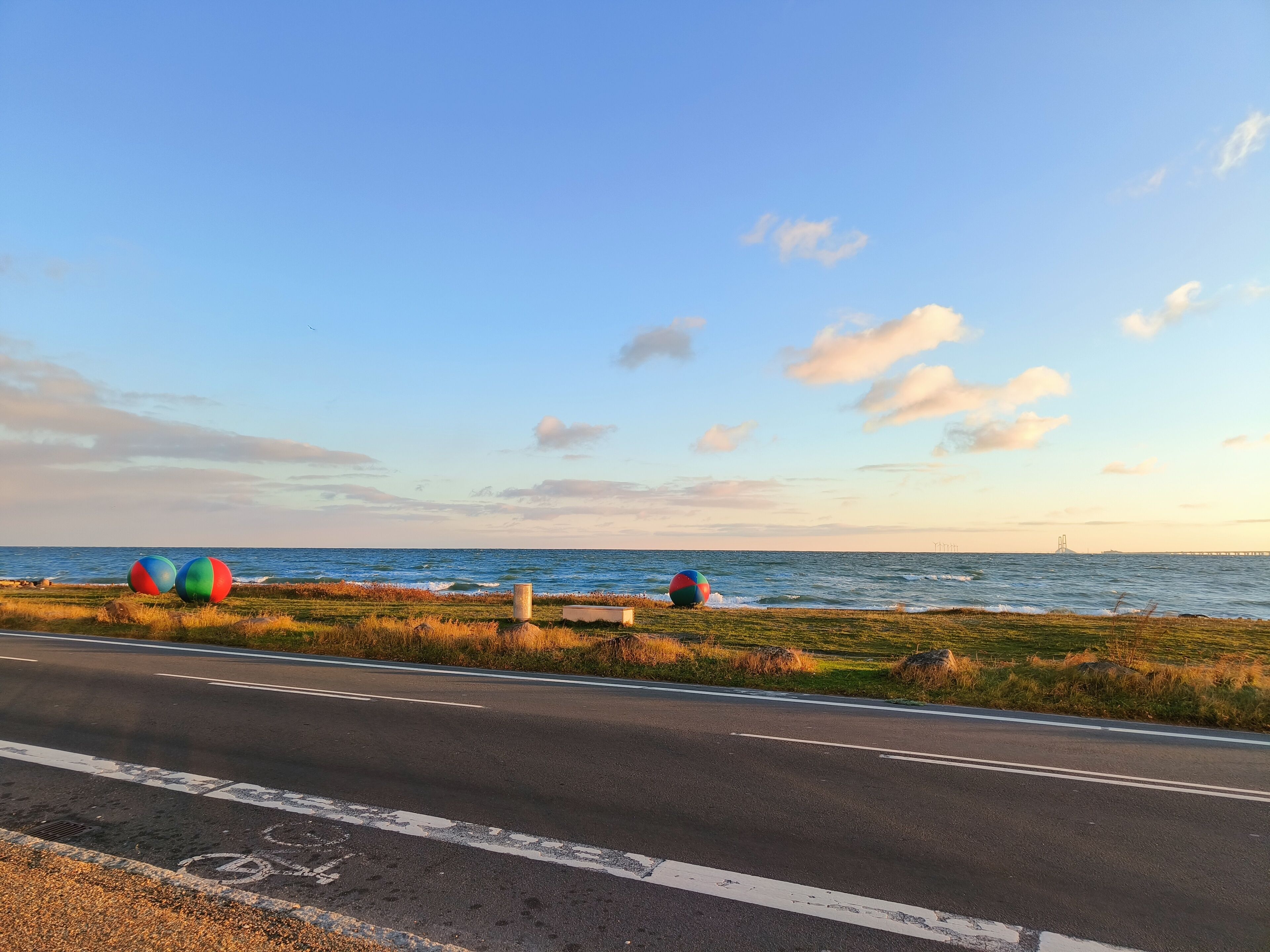 A coastal road with a clear view of the sea and a bridge in the distance.