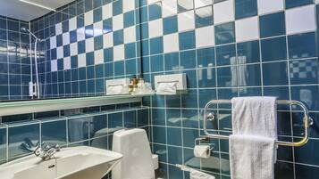 Et badeværelse med en hvid vask, toilet og et spejl. Væggene er fliset med et blåt og hvidt skakmønster.