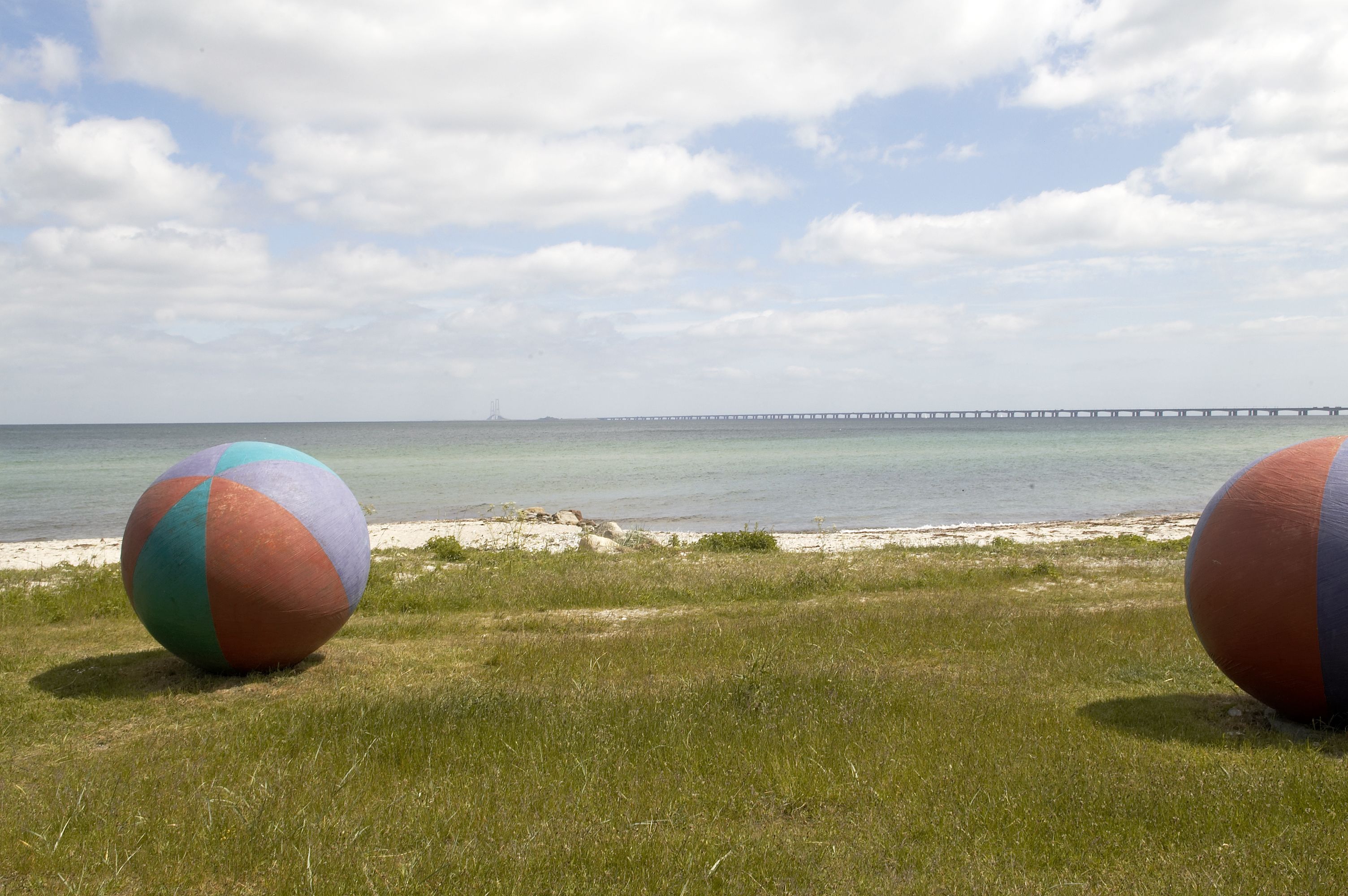 A beach with two large beach balls and a pier in the background.