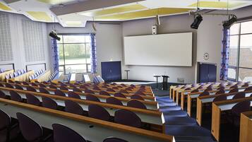 Un'aula con file di banchi e sedie, uno schermo di proiezione grande e una zona palco.